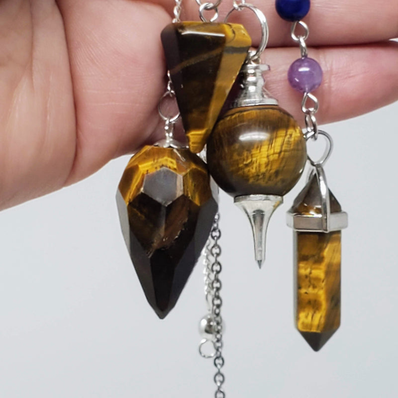 Tiger's Eye Pendulums draped over a hand on gray background.