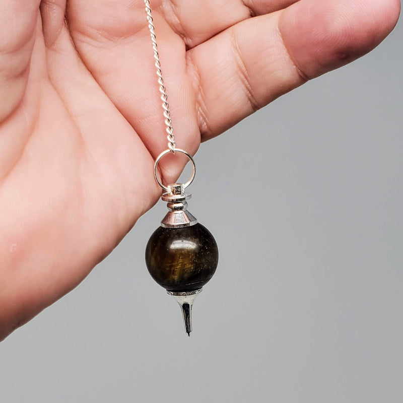 Tiger's Eye Pendulums draped over a hand on gray background.