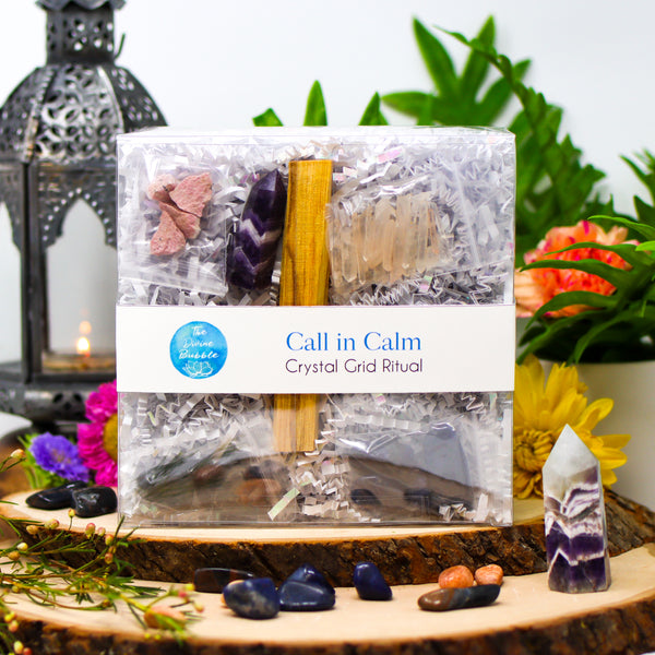 Magical display of Call In Calm Crystal Grid Ritual package and its contents, surrounded by flowers and a burning lantern